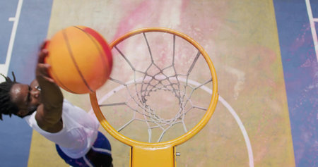 Leaping player white jersey blue shorts reaching rim, net with orange ball on painted park court....