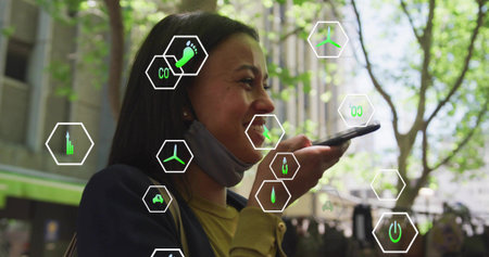 Speaking woman wearing jacket holding phone to mouth on city sidewalk mask under chin, eco icons....