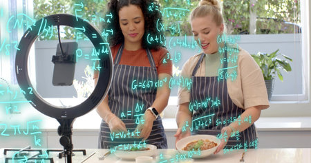 Recording two women plating food in home kitchen, in striped aprons with ring light. Cooking,...