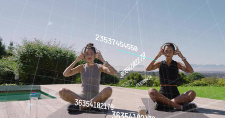 Adjusting over-ear headphones, two women in activewear following workout on deck by pool, AR grid....