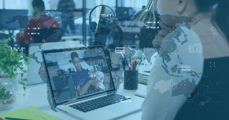 Showing laptop screen of remote woman wearing dark top, cradling fabric in open office, HUD overlay....