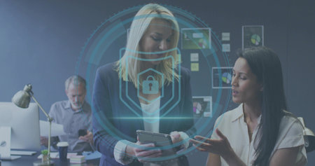 Holding tablet, blonde woman wearing blazer presenting security HUD in office, monitors visible....