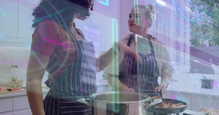 Cooking two women in striped aprons chopping and stirring in home kitchen with pot and pan. Duo,...