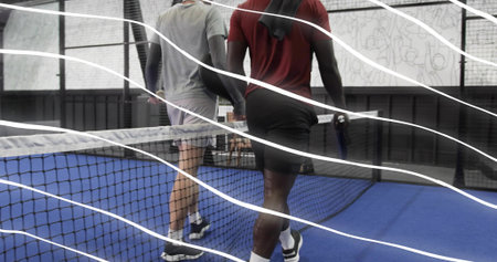 Walking two men in sportswear carrying rackets and towel across blue court, net foreground. Athletes, teammates, training, paddle, mural, facility, overlayの写真素材