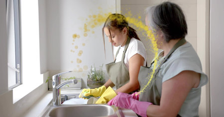 Washing women wearing green aprons yellow-pink gloves at home sink with stainless faucet and dishes....