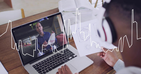 Viewing man wearing headset holding diagrams at home table with laptop waveform overlay, copy space....