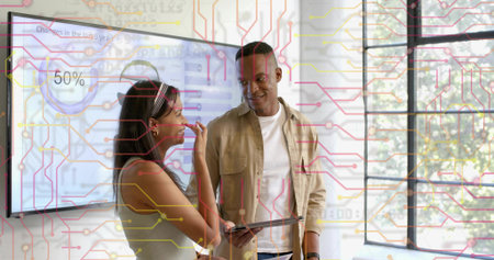 Two peers in tan shirt and headband reviewing 50% display in office holding tablet, circuit overlay. Collaboration, teamwork, modern, business, dashboard, charts, windowの写真素材