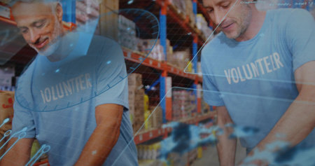 Sorting two men in blue VOLUNTEER-shirts leaning at warehouse table with boxes and digital overlay. Logistics, packing, organizing, inventory, shelving, teamwork, industrialの写真素材