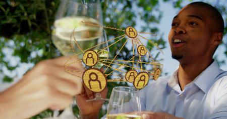Clinking man in light shirt laughing, raising white wine glass on patio. Friends, toasting, outdoor, terrace, daylight, greenery, bokehの写真素材