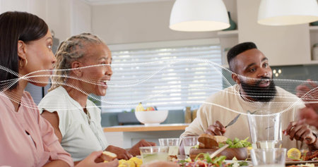 Sharing multigenerational family passing dishes at home dining table, woman in pink blouse speaking....