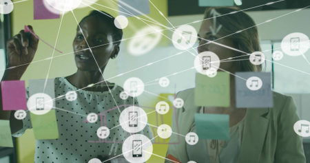 Pointing woman with marker at office glass partition of sticky notes, app icons, in polka-dot top....