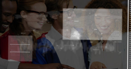 Smiling group of classmates wearing gown and glasses, leaning in room, viewing tablet with overlays....
