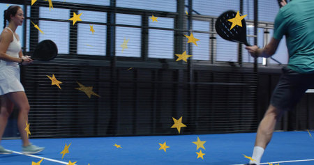 Preparing man in teal shirt swinging perforated paddle racket on blue padel court, mesh fence. Athlete, competitor, rally, surface, facility, focus, dynamicの写真素材