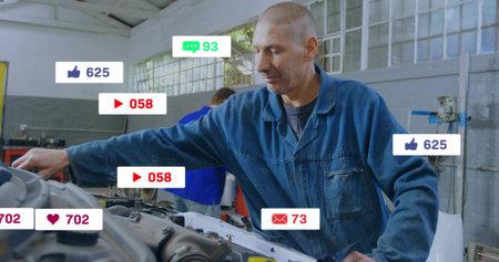 Inspecting mechanic wearing blue coveralls reaching into open engine bay at garage. Technician, car,...