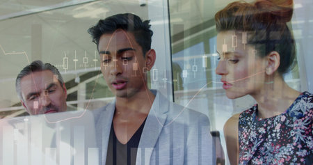 Analyzing three professionals leaning over laptop in office, gray blazer man pointing at charts....