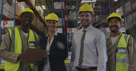Standing at pallet racks staff and lead in blazer wearing yellow hard hats, vests holding clipboard. Warehouse, team, supervisor, manager, helmet, highvisibility, inventoryの写真素材
