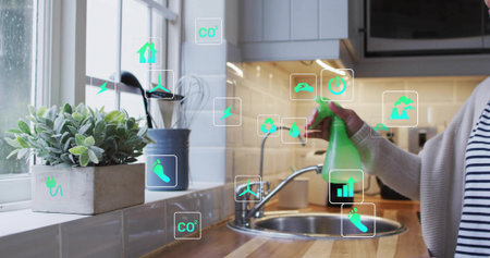 Spraying woman in cardigan and stripes at kitchen sink with green bottle, copy space. Eco,...