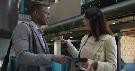 Discussing colleagues in blazers sharing ideas in atrium, with tablet, shoulder bag, blue overlay....