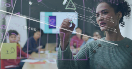 Writing woman in green sweater marking glass board meeting room, with marker and laptop, copy space. Collaboration, brainstorming, teamwork, workshop, boardroom, office, ideationの写真素材