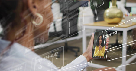 Woman in white-top and gold-earring holding phone showing coworker in yellow at office, copy space. Smartphone, screen, ui, overlay, wireframe, collaboration, virtualの写真素材