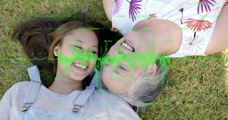 Lying family smiling on grassy lawn, wearing denim overalls, striped, floral tops, green waveform....