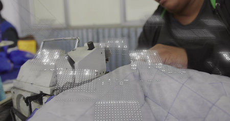 Operating industrial sewing machine, woman guiding quilted fabric in workshop wearing blue jacket....