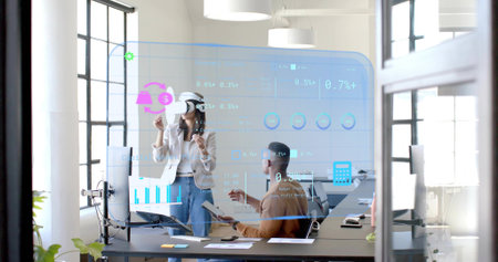 Colleagues wearing blazers using holographic UI on glass wall in office with AR headset, tablet....