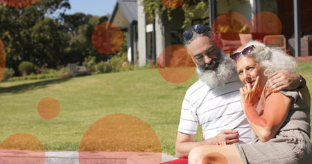 Sitting senior couple embracing on stone edge in yard sunnies watch clothes orange dots, copy space....