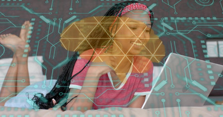 Smiling woman with braids wearing pink tee and red headband watching laptop on bed, circuit overlay....