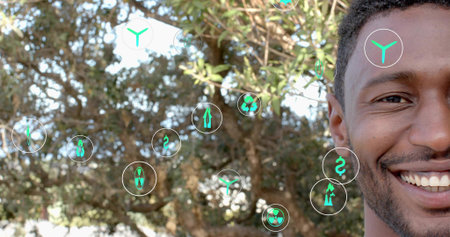 Smiling man with curly hair and beard standing in park, displaying floating UI icons, copy space....