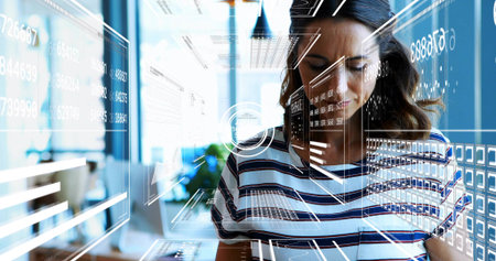Tapping laptop, woman in striped shirt working at modern office with holographic overlays and plant....