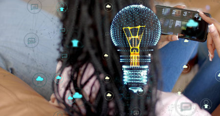 Scrolling braided woman in blue top holding smartphone at home, with holographic lightbulb icons....