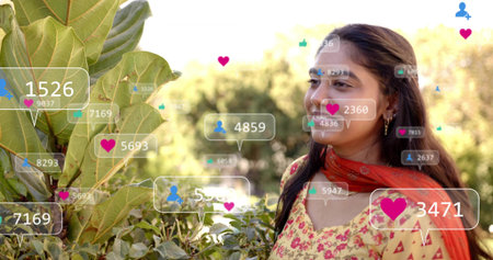 Smiling Indian woman in floral-kurta orange-dupatta by garden foliage, copy space. Model, outdoor,...
