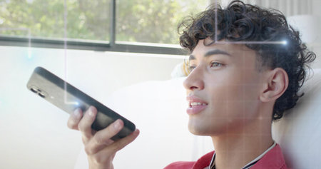 Holding black smartphone, male wearing red top reclining on light couch near window, copy space....