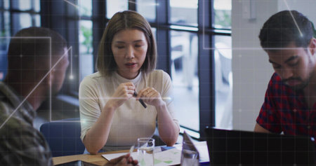 Reviewing charts mid adult Asian woman holding pen in meeting room, in ribbed top, laptop nearby....