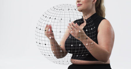 Presenting adult woman wearing black crop top and black bottoms holding wireframe globe in studio....