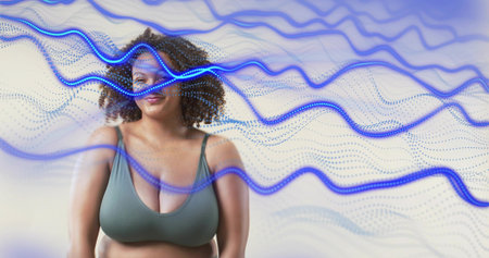 Standing woman wearing muted green sports bra posing in studio, with blue wavy overlays. Portrait,...