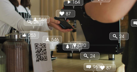 Handing barista in dark apron and white top holding reader at cafe counter, phone, social icons....