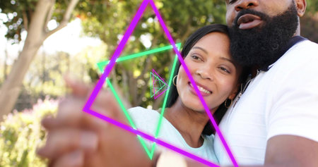 Leaning couple sharing hug in park, with neon overlays, blurred clasped hands, blue top, white polo....