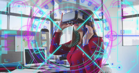 Adjusting seated woman in red blouse using VR headset at office desk, with HUD graphics. Virtual,...