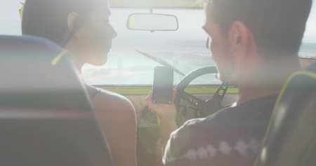Holding smartphone, couple leaning toward screen in coastal car, woman sleeveless top, man dark tee....