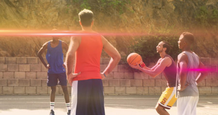 Playing men in tanks and shorts, passing ball on outdoor court with orange basketball, brick wall....