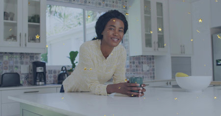 Smiling adult woman wearing patterned blouse leaning on white island at home, holding teal mug. Cheerful, kitchen, daylight, modern, bright, countertop, coffeeの写真素材