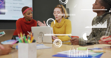 Leading woman in mustard turtleneck speaking and gesturing in meeting room, with laptop and screen....