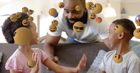 Smiling father leaning over sofa, playing with children in pink and grey, floating emoji spheres....