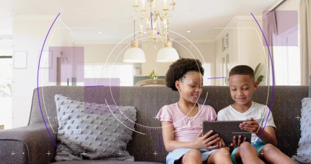 Sharing tablet, two children sitting on dark gray sofa in modern living room, holding tablet. Couch,...