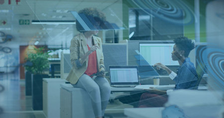 Discussing colleagues in blazer and jacket at modern office pointing at monitor with smartphone....