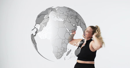 Reaching woman in black athletic crop top touching semi-transparent globe in studio, copy space. Orb, female, athleticwear, minimalist, highkeyの写真素材