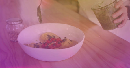 Drizzling woman in light long-sleeve spooning pesto from glass jar onto pasta at home, white bowl....