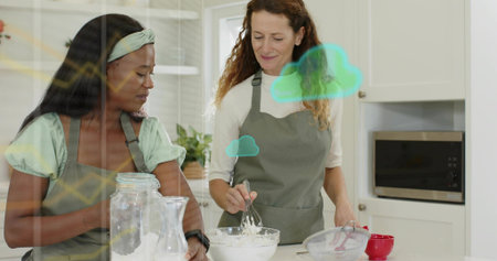 Whisking, two women wearing grey aprons preparing batter at kitchen island, with glass jar of flour....